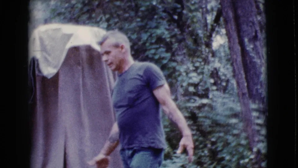 A man in a blue t-shirt and jeans walks past the tent in the 1968 Cottonwood, Arizona home-movie scene.