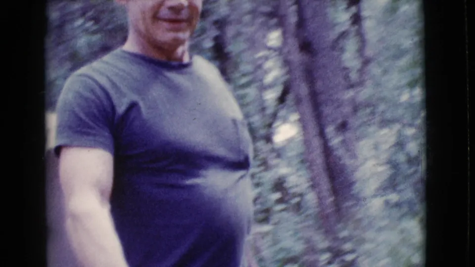 Close 8mm frame of an adult man in a dark T-shirt moving through wooded Cottonwood, Arizona surroundings in 1968.