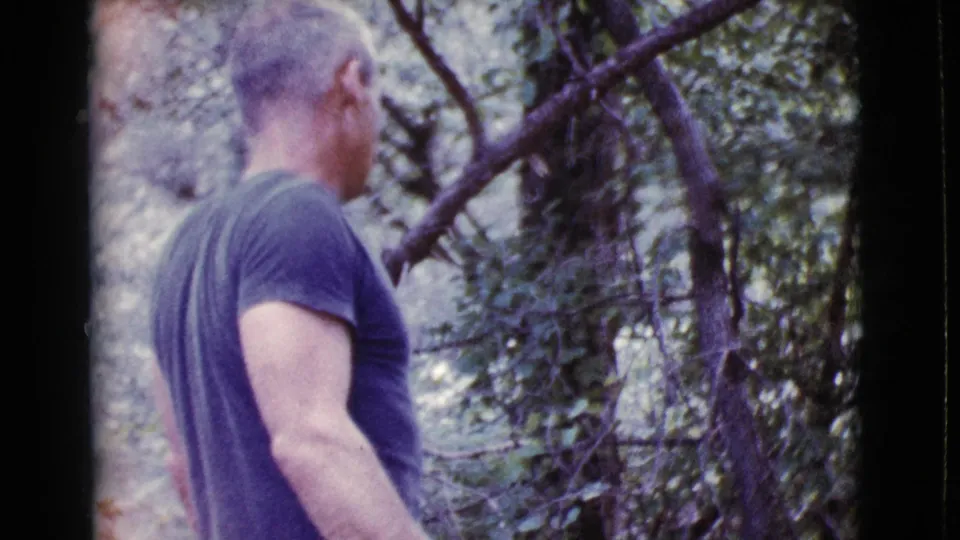 Side and rear view of the man in a blue shirt among green trees in 1968 Cottonwood, Arizona footage.