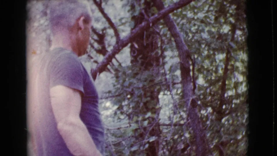 The man remains partly side-on among trees, with the 8mm frame showing soft color and handheld composition.