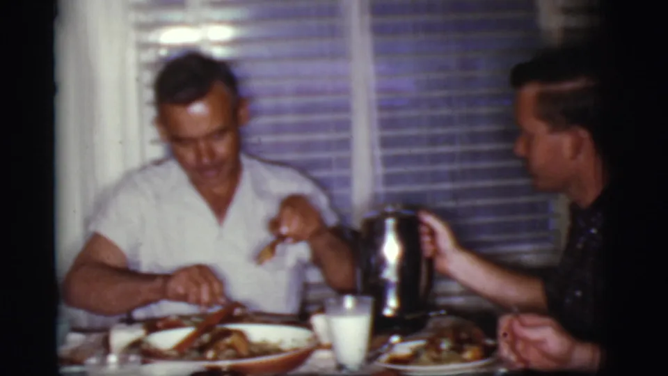 1968 Cottonwood, Arizona home-movie frame of men eating breakfast at a table with plates, cups, food, and a metal coffee pot.