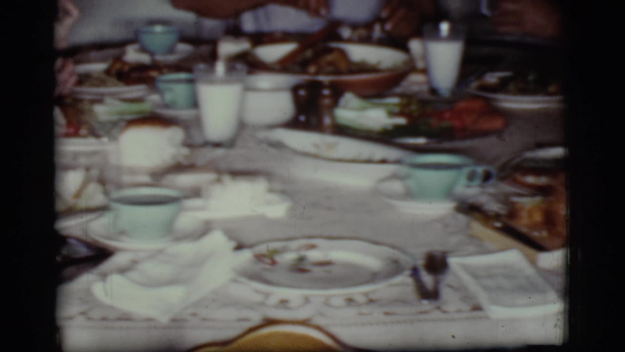 Lace-covered dining table with plates, milk glasses, cups, and food during a family meal.