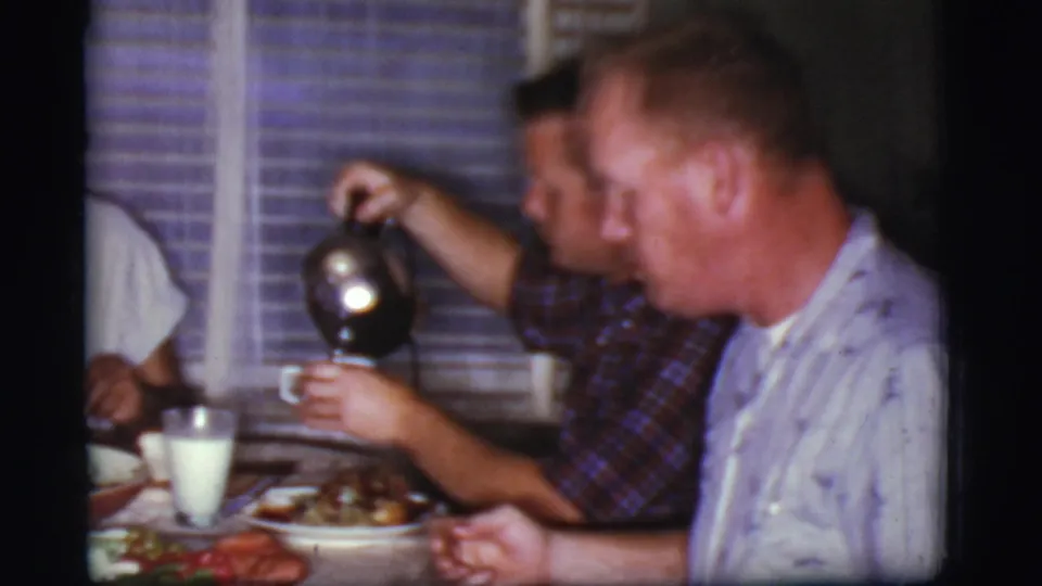 1968 Cottonwood, Arizona dinner-table frame with adult men, coffee being poured, plates of food, milk glasses, and blinds behind them.
