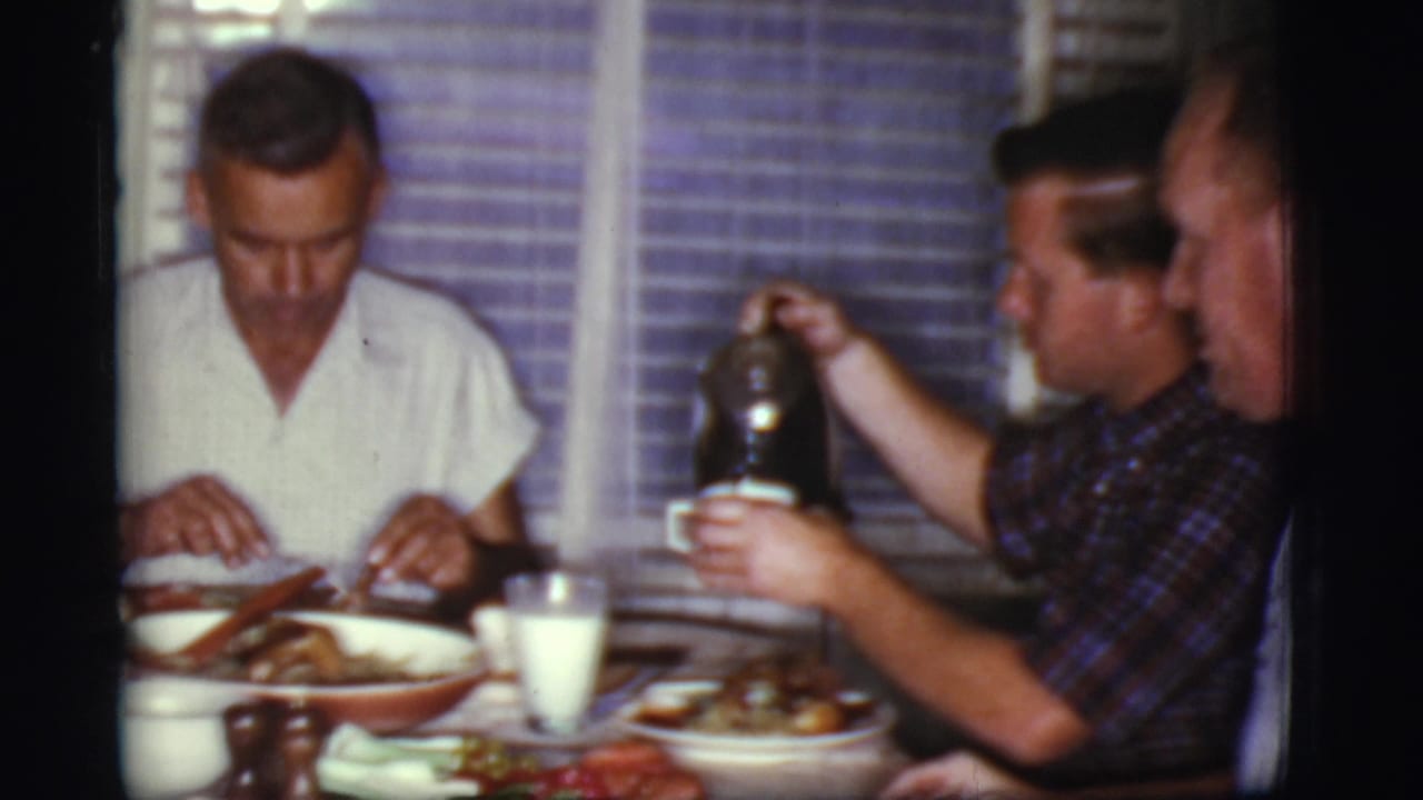 Men seated around a dining table with breakfast dishes and a glass of milk.