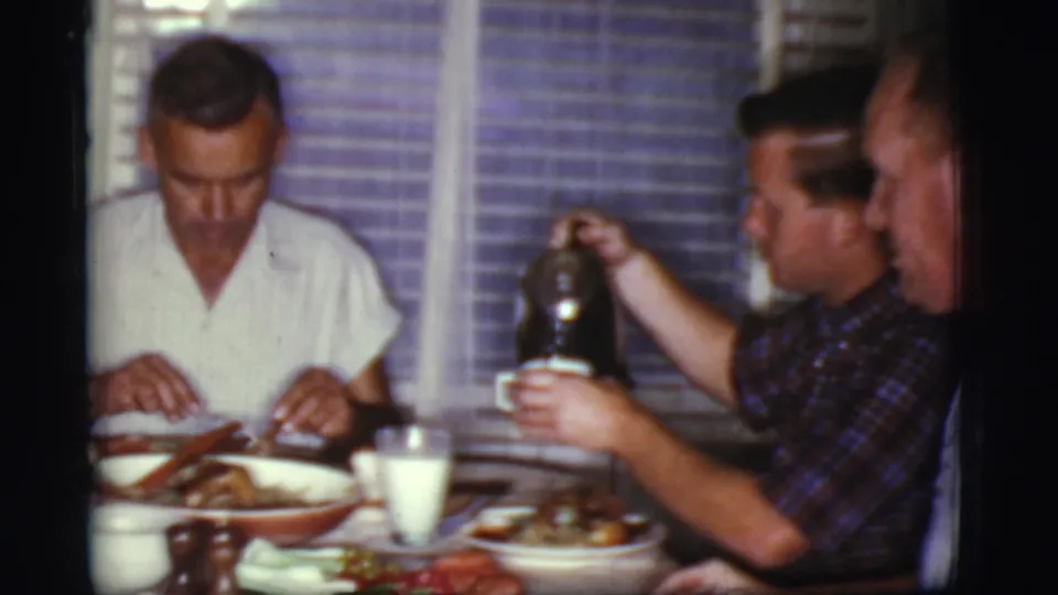 In a 1968 Cottonwood, Arizona home-movie frame, men sit at a dining table while one handles a dark coffee pot near breakfast dishes.