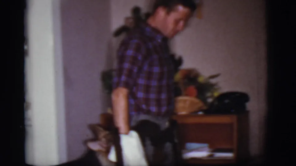 A man in a plaid shirt stands in a Cottonwood, Arizona interior as a German Shepherd follows closely beside him.