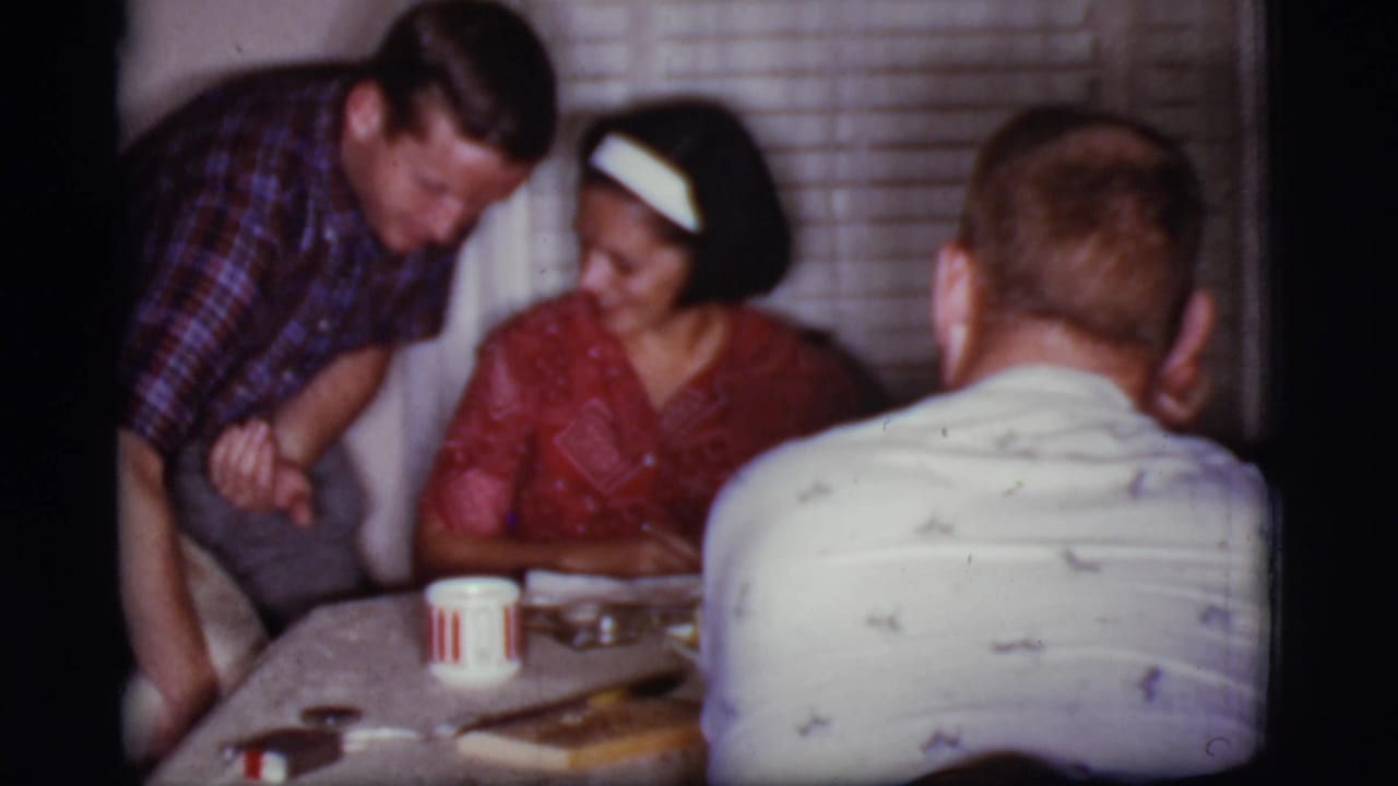 Adults around a dinner table as a man leans toward a seated woman.