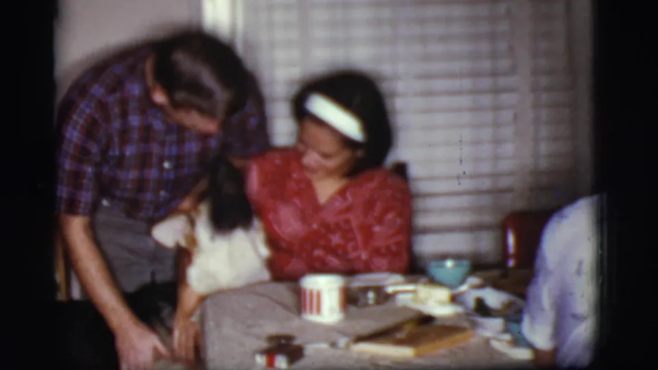 1968 Cottonwood, Arizona home-movie frame of adults petting or holding a dog near a dining table in a private room.