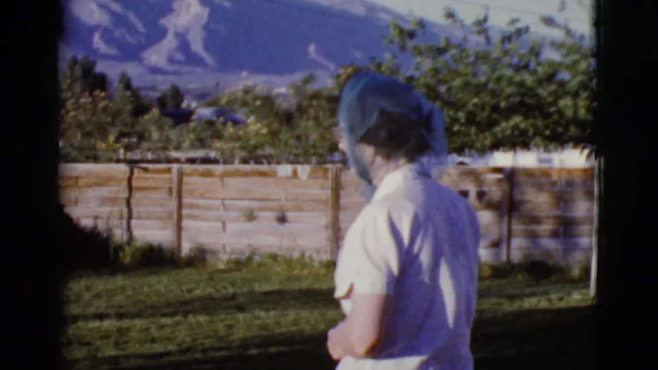 The woman remains turned away in the Cottonwood, Arizona yard, framed by grass, trees, a block wall, and mountain slopes.
