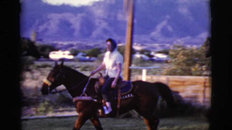 The rider continues through the Cottonwood, Arizona yard in 1968, passing a wooden fence and utility pole with mountains beyond.