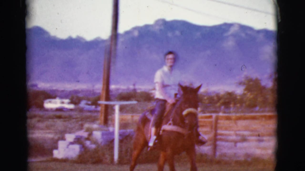 Woman riding a horse on rural property with mountains behind her.
