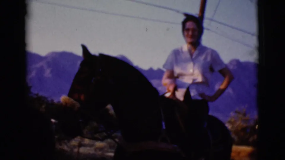 A woman in a light shirt sits on a dark horse against the Cottonwood, Arizona mountain landscape in 1968 home-movie footage.