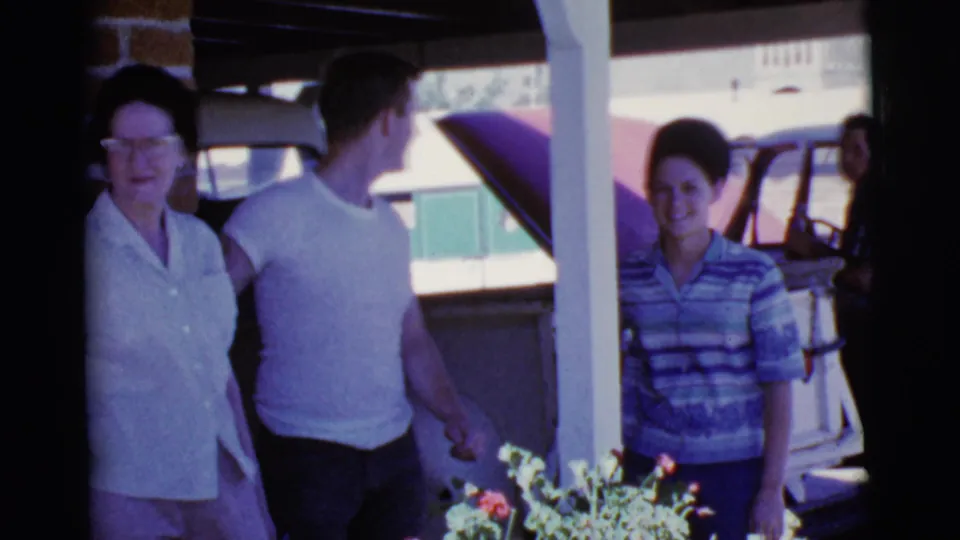 Family members in Cottonwood, Arizona, stand beneath a carport beside vintage cars in a 1968 8mm home-movie frame.