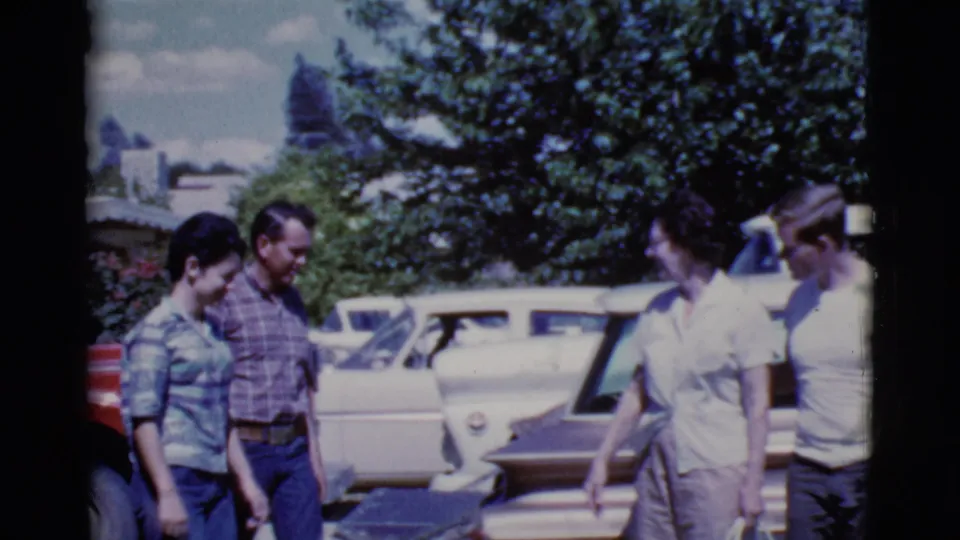 Four adults gather beside classic parked cars in Cottonwood, Arizona, with trees behind them and visible 8mm color grain.