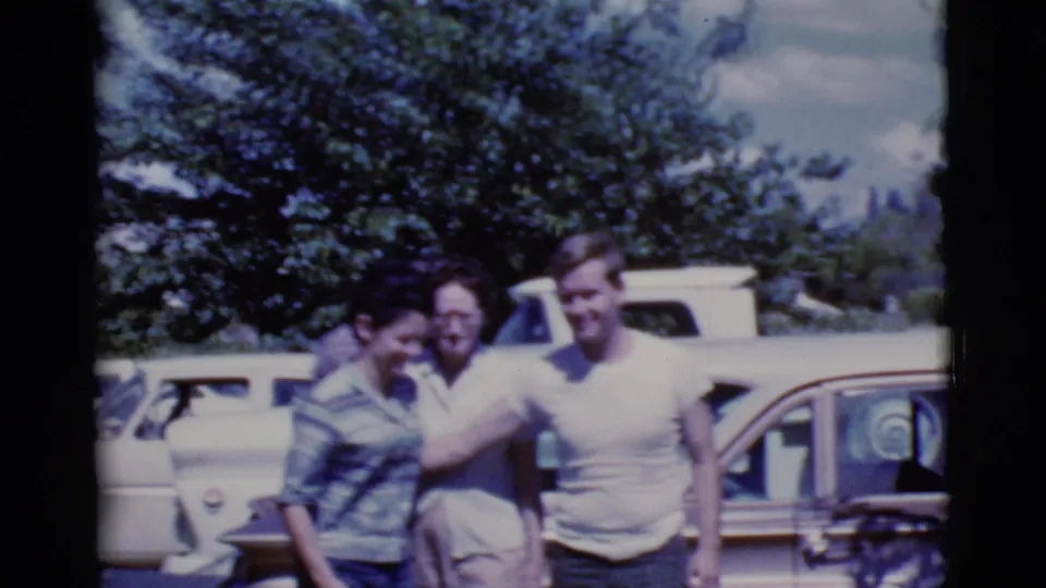 Three adults stand shoulder to shoulder beside parked cars in Cottonwood, Arizona, captured with soft 8mm home-movie texture.