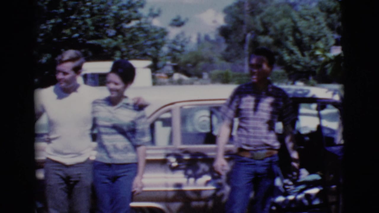 Young adults standing beside a light-colored car in a sunny outdoor parking area.