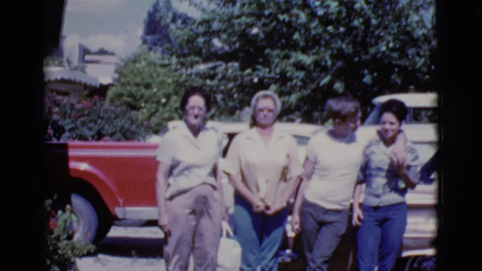 A 1968 Cottonwood home-movie frame shows four people centered beside a brown car, with another figure partly cropped at the right edge.