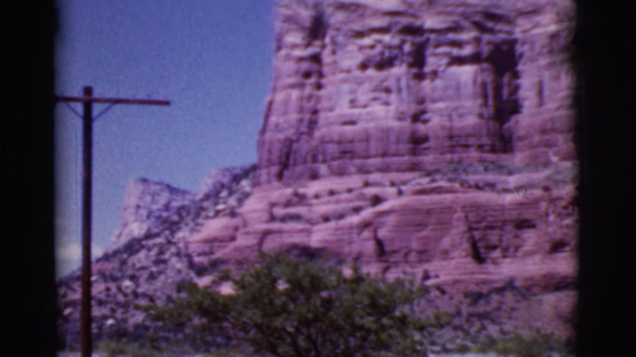 Red rock formation beside a utility pole under a blue desert sky.