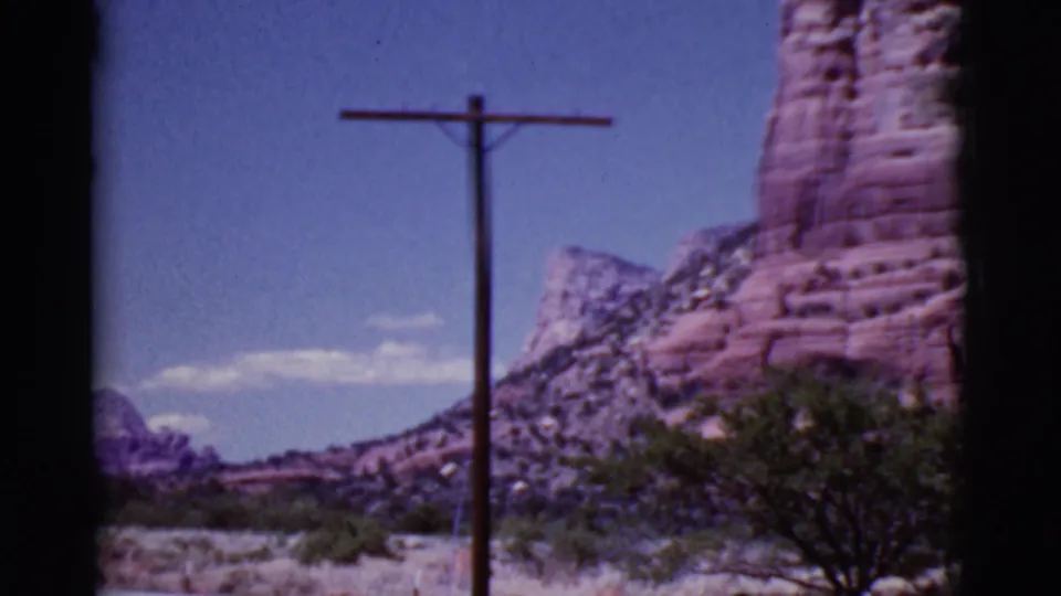 Cottonwood, Arizona home-movie frame with a utility pole centered before layered red cliffs, desert vegetation, and distant hills.