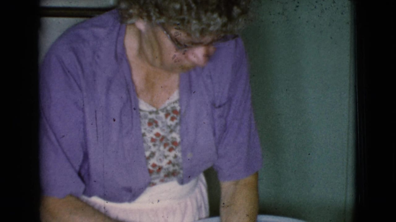 Older woman in purple cardigan looks down while working near a bowl indoors.
