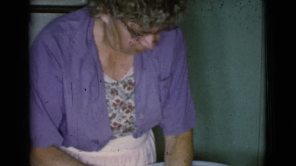 In 1968 Cottonwood home-movie footage, an older woman in a purple cardigan and glasses looks down during a household task.