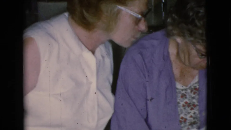 Inside a private Cottonwood interior, a woman in white observes an older woman in purple leaning over a bowl or basin task.