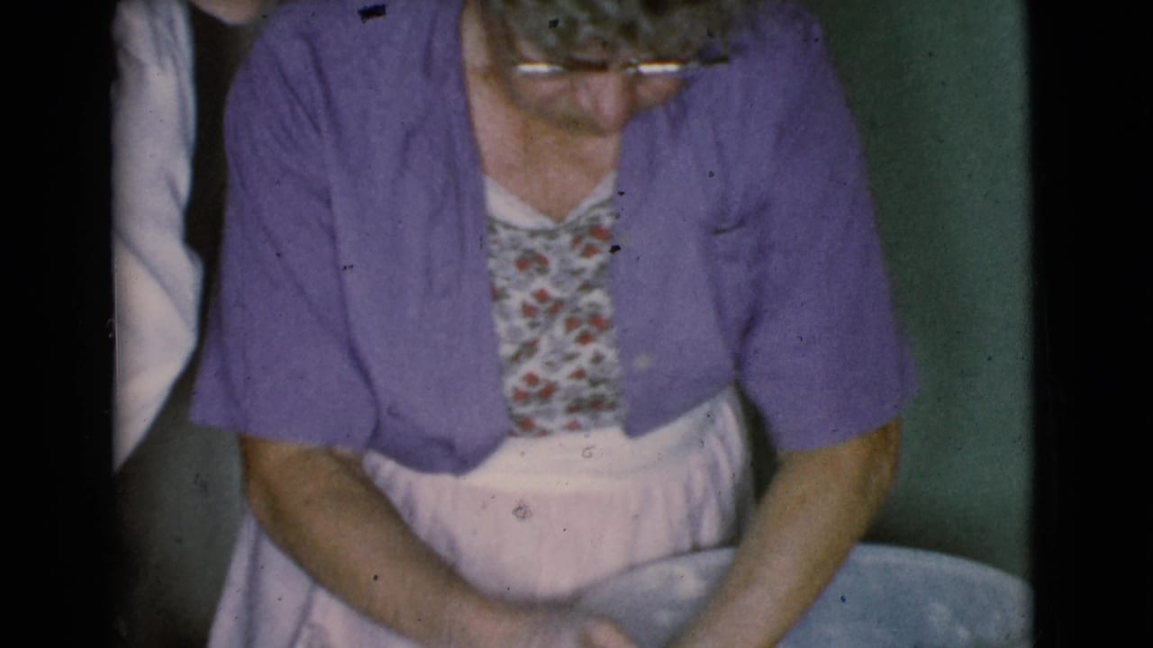 Older woman in a purple cardigan works over a large bowl in a domestic interior.