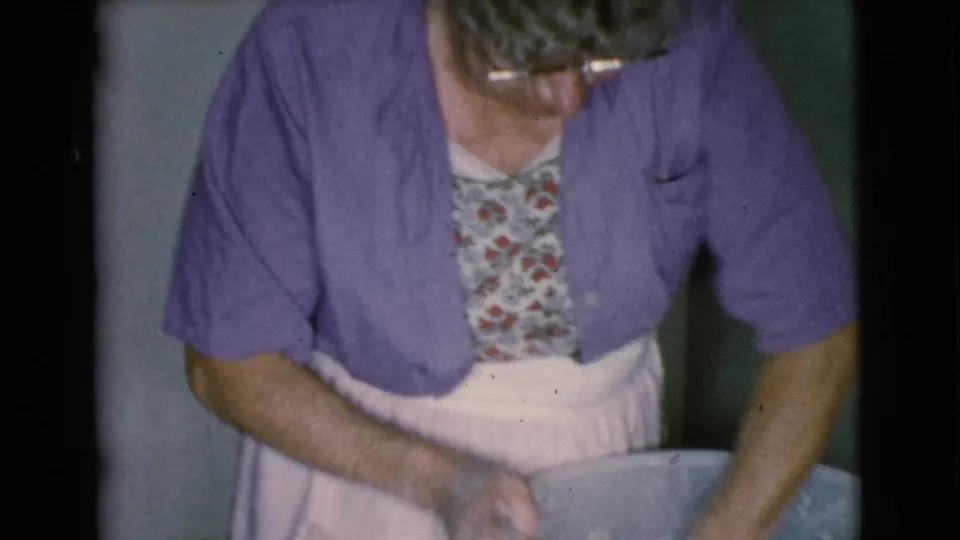 A close home-movie view shows the woman leaning over a large bowl, apparently kneading dough in the 1968 kitchen scene.