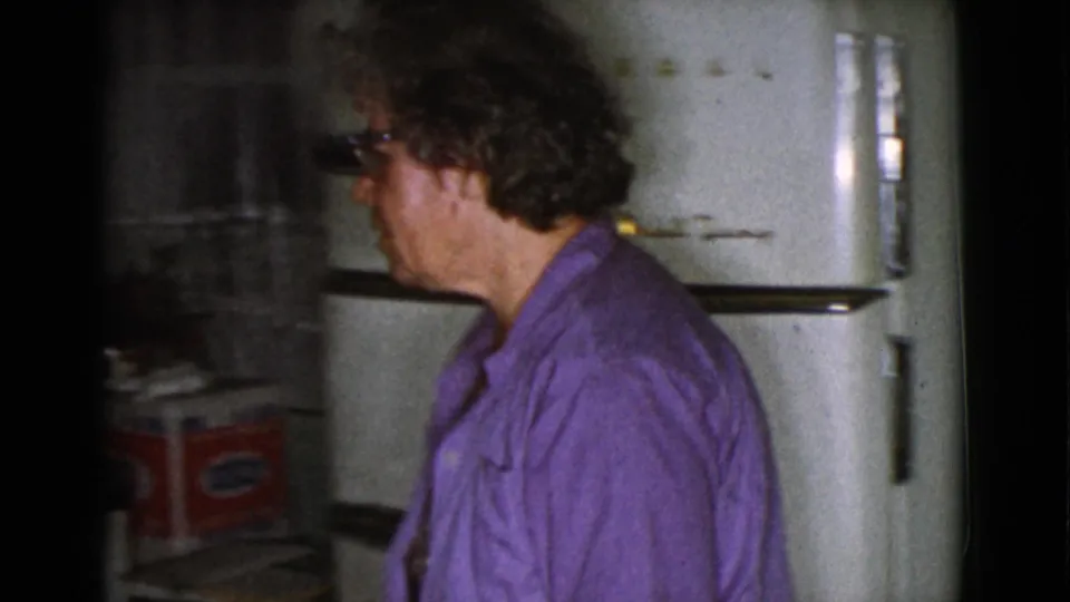 A woman in glasses and a purple cardigan stands in profile beside a rounded white refrigerator in the Cottonwood kitchen.