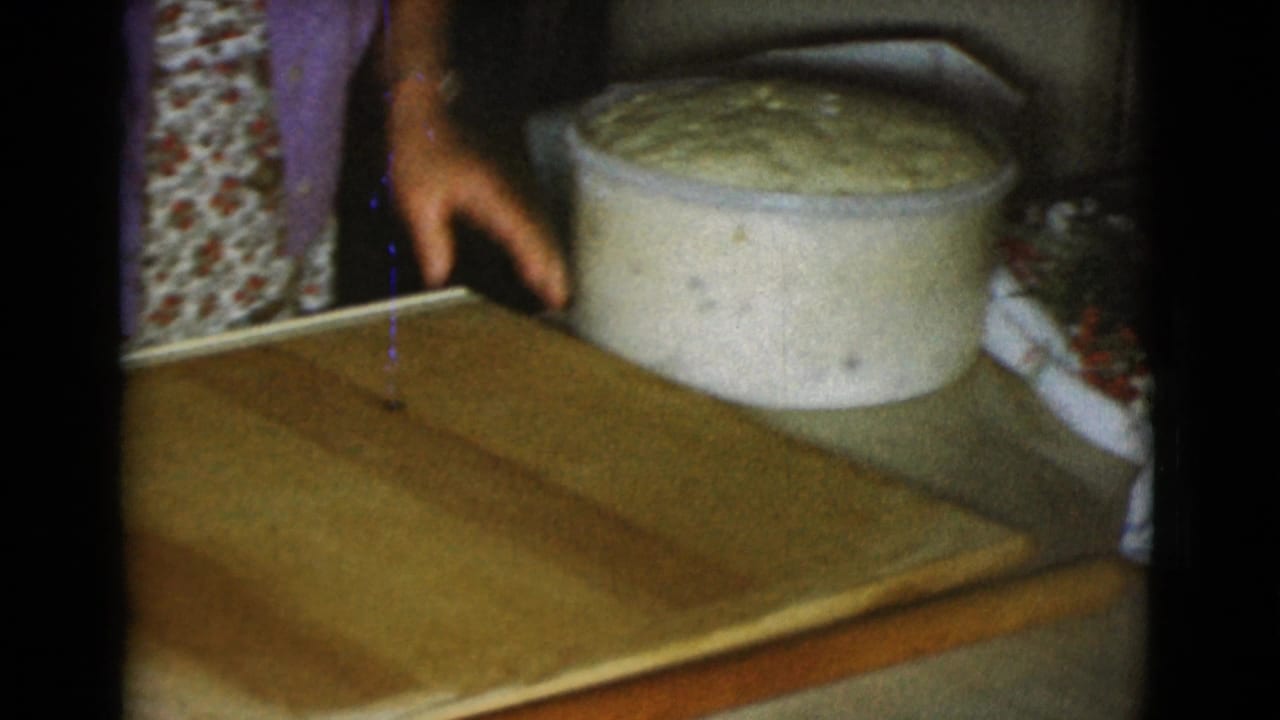 Woman's hands near a wooden board with a large bowl of risen dough behind it.