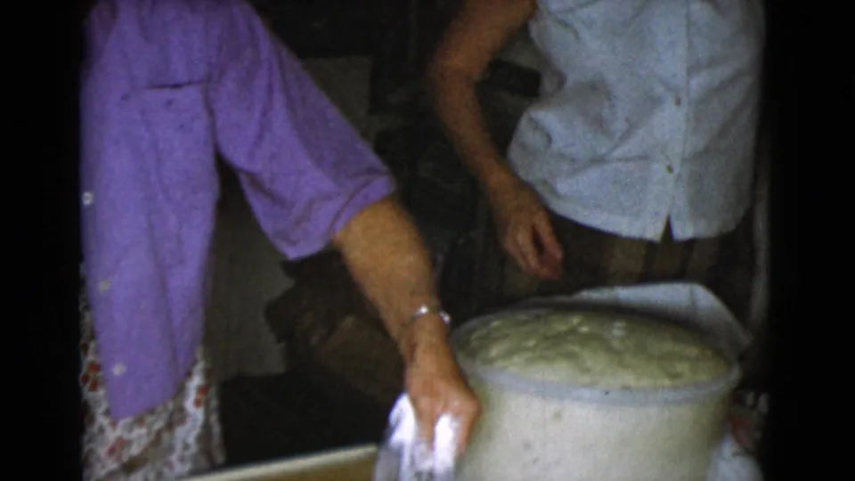 1968 Cottonwood, Arizona home-movie frame with a woman reaching near a dough bowl and another adult partly visible beside her.