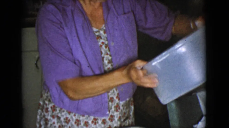 In the home kitchen, the woman lifts or tilts a large light-colored bowl or pan, consistent with the dough preparation described in the clip metadata.