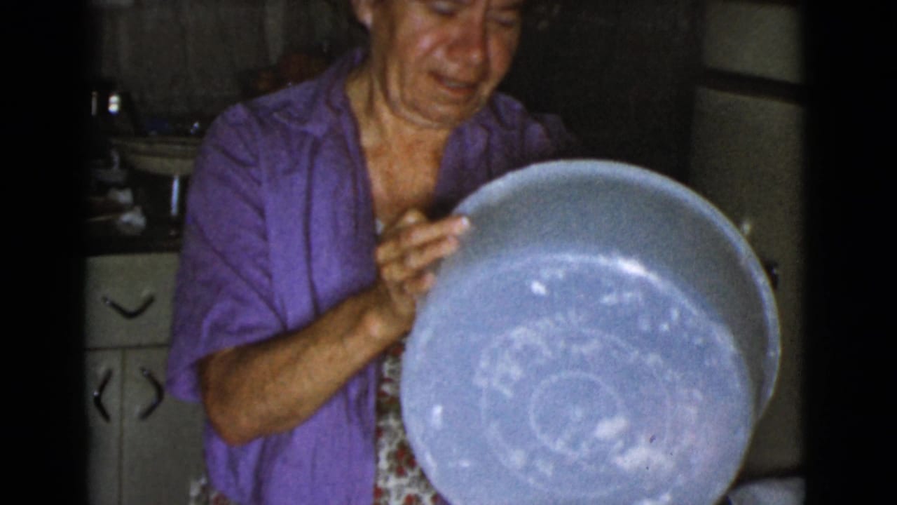 Woman in a purple shirt holds a large floured bowl in a kitchen.