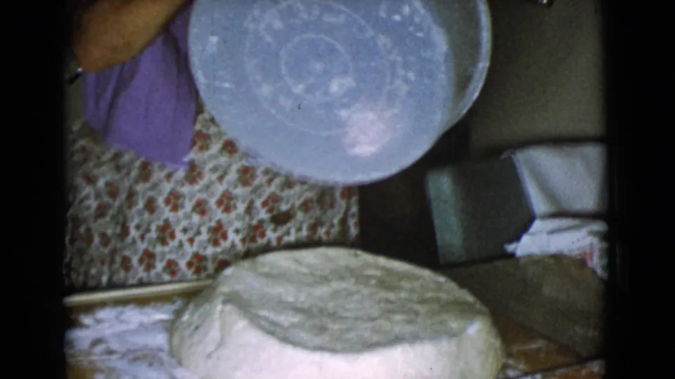 A large round of dough sits on a floured wooden board while the woman holds the bowl above it in the 1968 home kitchen scene.