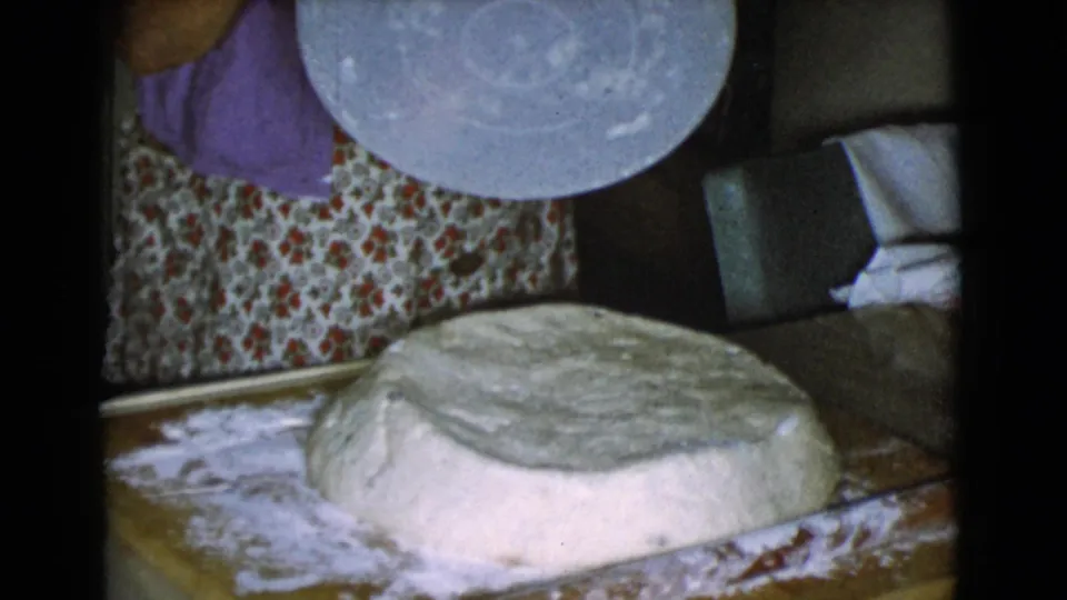 The woman in a purple shirt stands near a large round of dough on a floured board inside a Cottonwood, Arizona home kitchen.