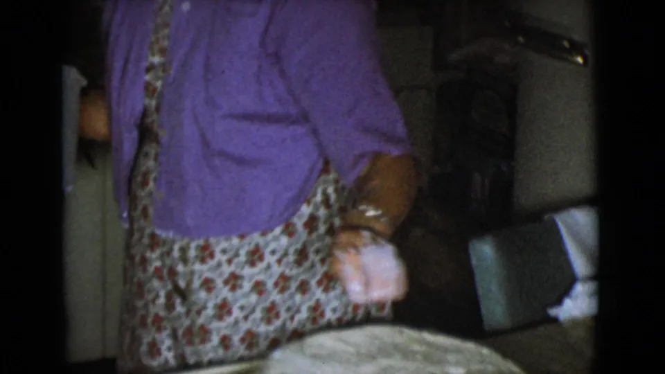 A woman in a purple shirt holds a flour-covered hand near a round of dough on a floured board in the 1968 kitchen footage.