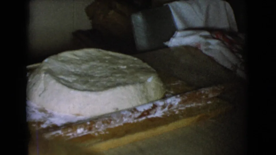 Bread dough remains on a floured wooden board, with soft 8mm exposure showing the private kitchen behind it.