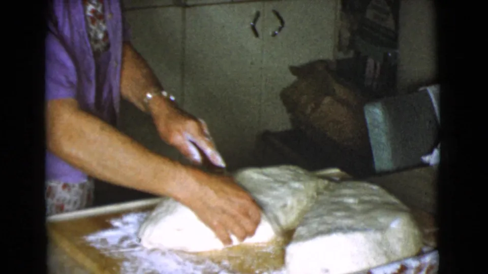 The woman folds or positions a large dough piece on a floured surface inside the Cottonwood kitchen.