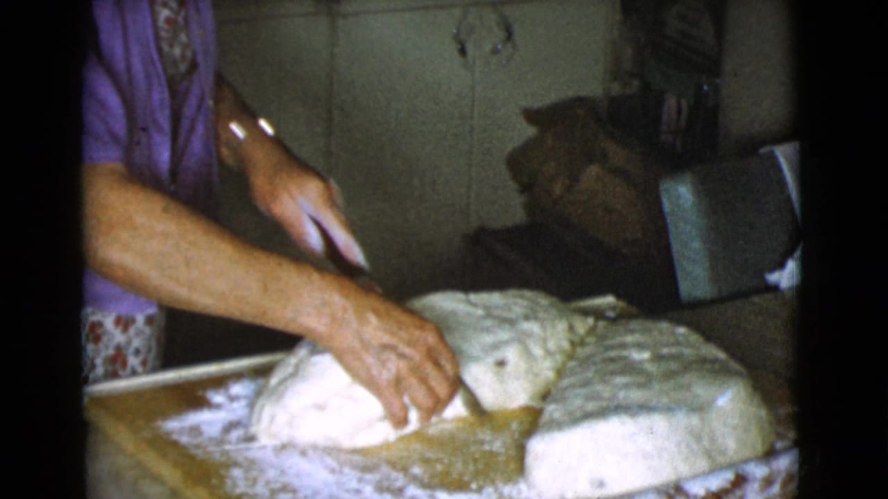Woman's hands cutting dough on a floured wooden board in a kitchen.