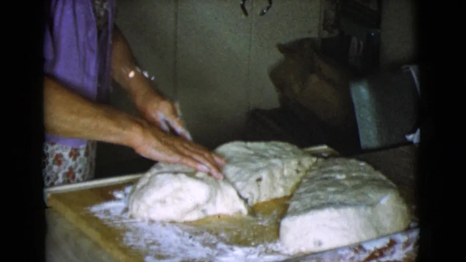 The woman's hands press a rounded dough piece on a floured board, with additional dough set nearby in the 1968 kitchen scene.