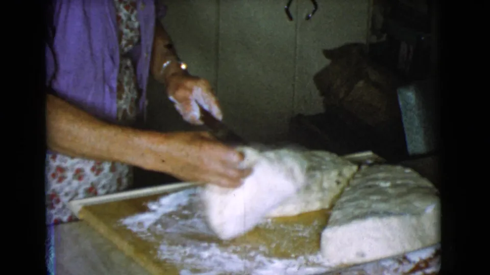 A woman lifts a portion of bread dough on a floured board in a 1968 Cottonwood, Arizona kitchen scene.
