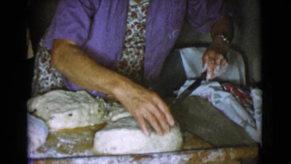 A woman in a purple shirt reaches over bread dough while holding a knife during home baking in Cottonwood, Arizona in 1968.