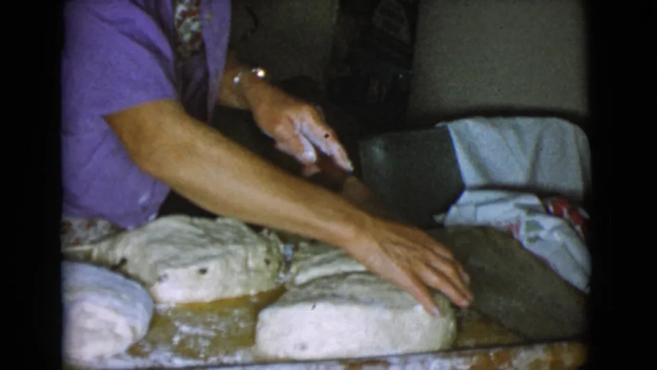 The woman reaches across shaped dough portions on a floured wooden surface during a 1968 Cottonwood, Arizona kitchen scene.