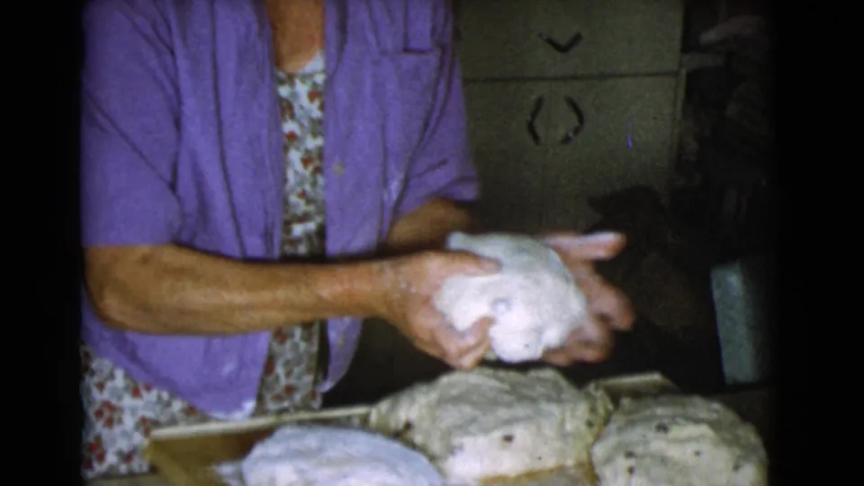 The woman holds a rounded dough portion above the work surface, with other loaves visible in the 1968 home kitchen scene.