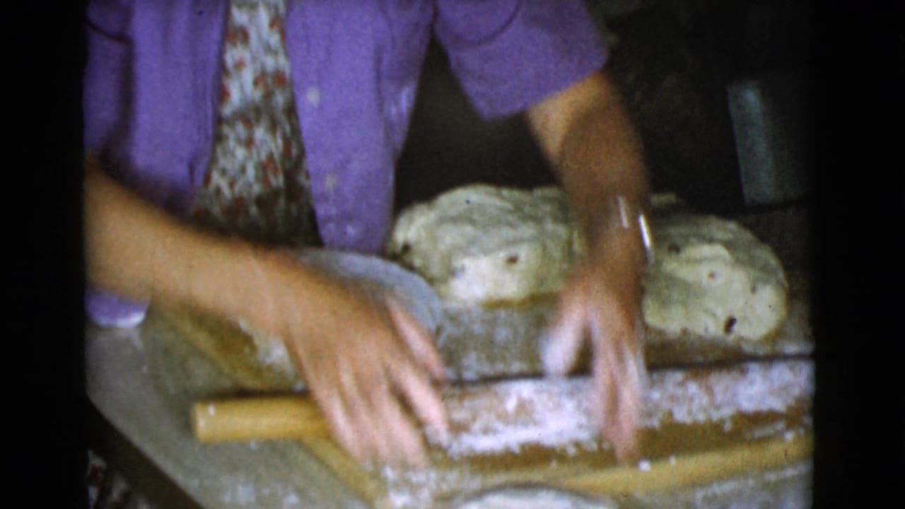 Hands shape dough on a floured wooden board with a rolling pin nearby.