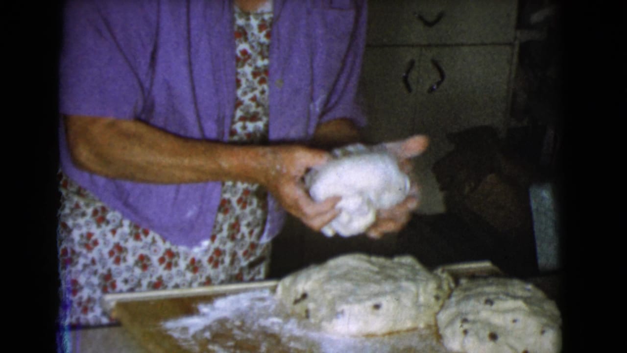 Older woman holds a ball of dough over a floured wooden work surface.