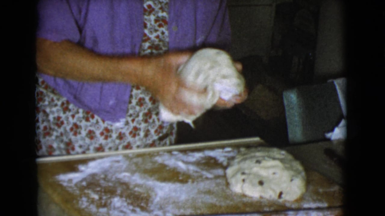Woman in a purple shirt kneads dough on a floured board in a kitchen.