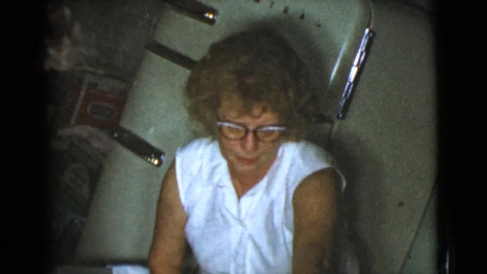 In Cottonwood, Arizona home-movie footage from 1968, an older woman in glasses sits near kitchen fixtures in a private interior.