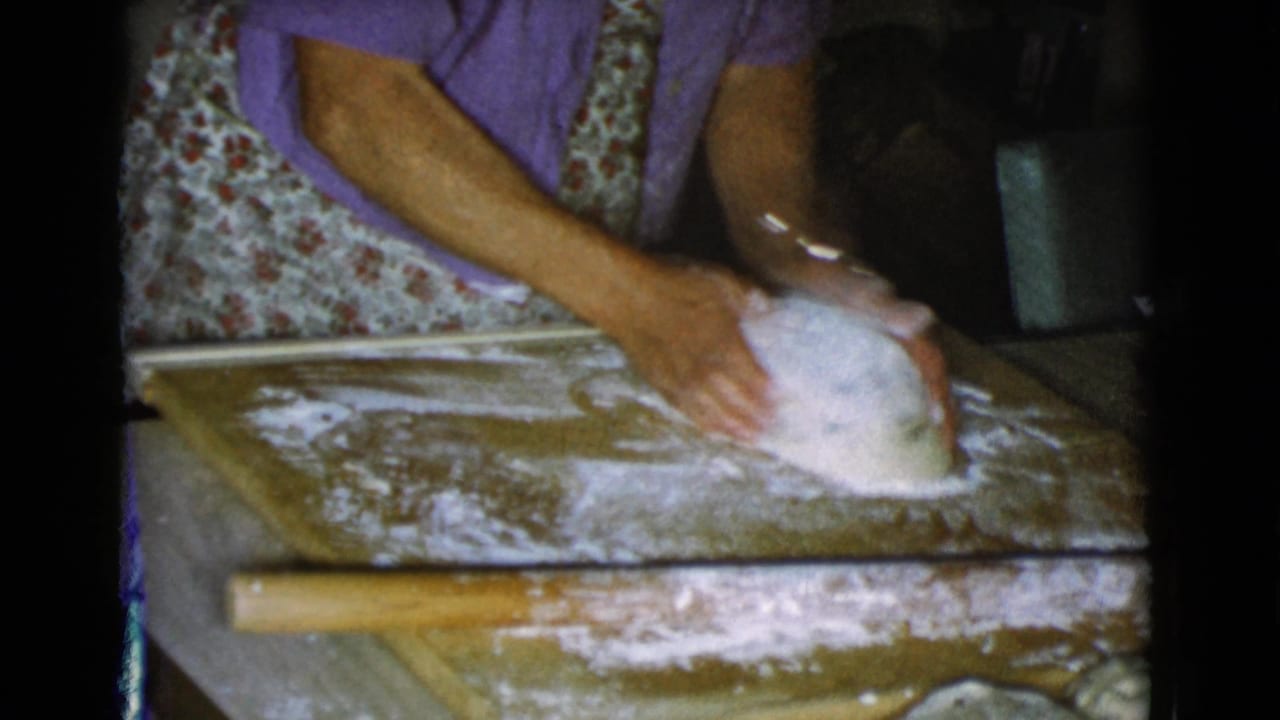 In 1968 Cottonwood, Arizona home-movie footage, a woman in a purple shirt and floral apron kneads dough on a floured wooden board.