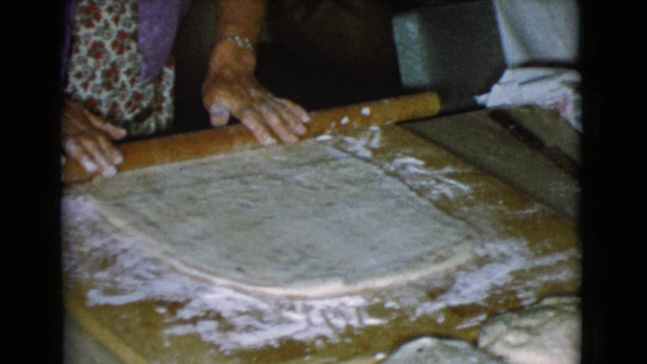 Hands use a rolling pin to flatten dough on a floured board.